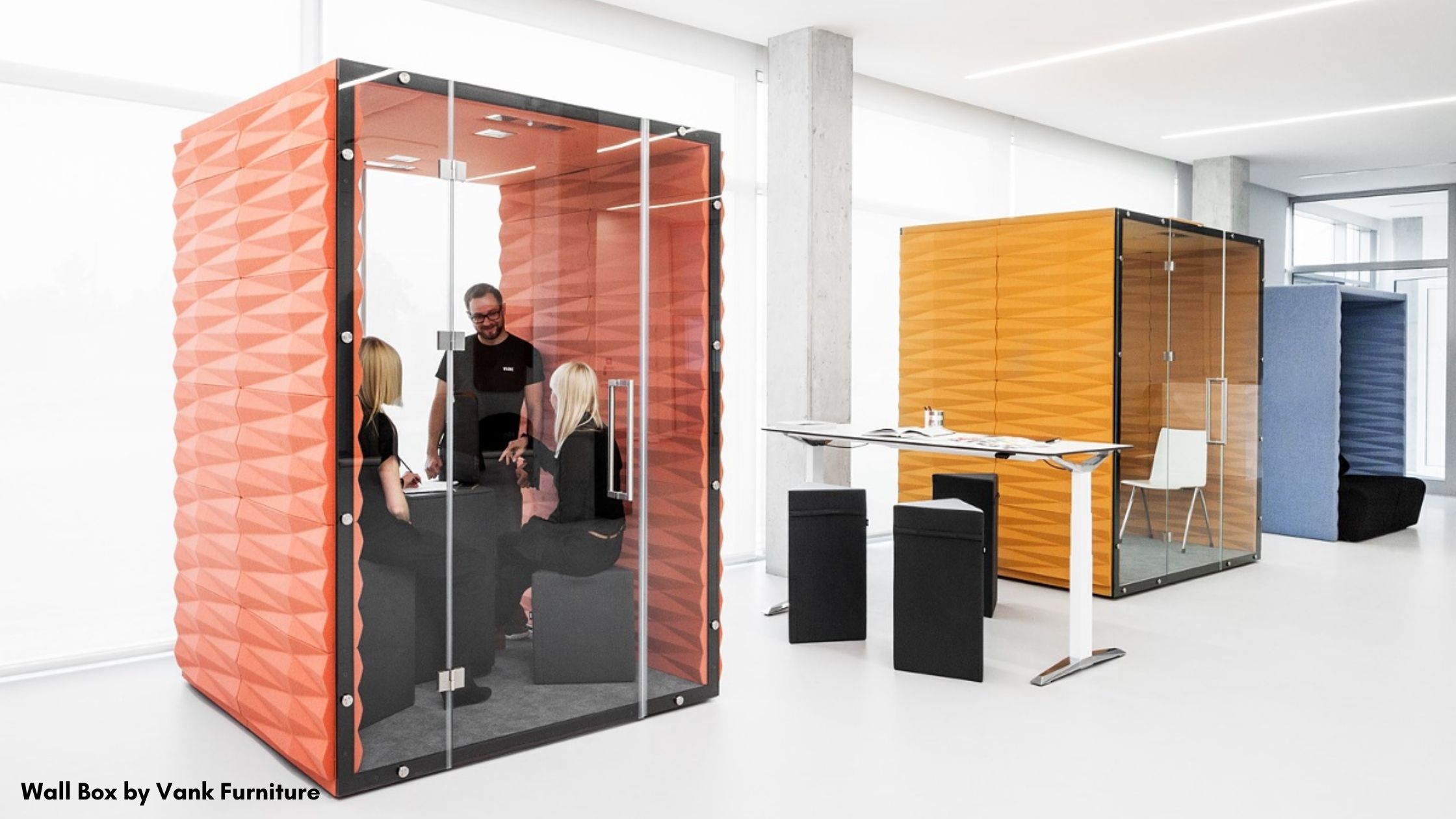 People having a meeting in an an office pad made of orange acoustic panels and glass. 