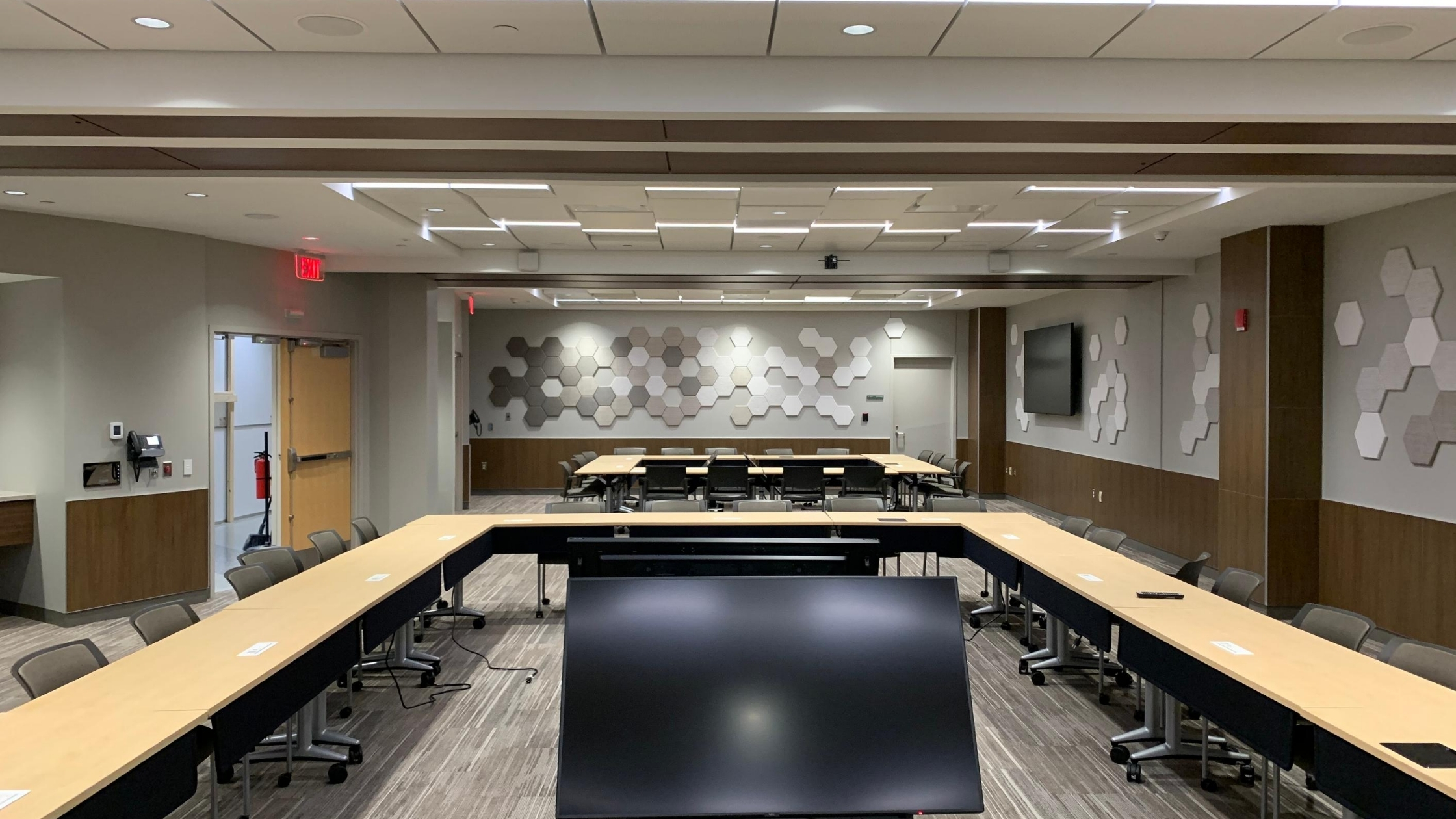 Office meeting room with two Skyfold operable partitions recessed in the ceiling and with hexagonal acoustic tiles on the wall. 